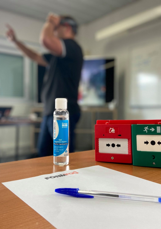 différents boitiers d'alarme disposé sur une table avec un papier et stylo pour la prise de note pendant que le formateur fait une démonstration sur le casque de réalité augmentée